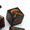 A D6 dice, black with bright orange Halloween faces on each side. Orange inked numbers. Dice sits on a white background.